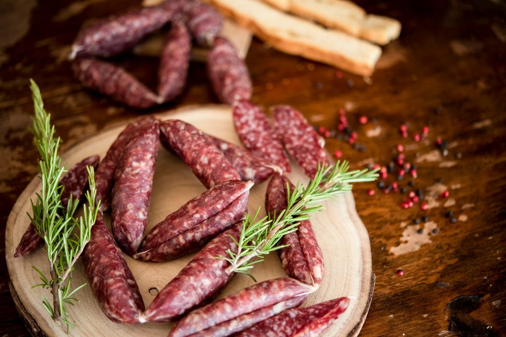 Artisanal sausages served on a wooden cutting board with fresh rosemary and crusty bread.